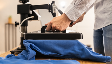 A person using a heat press on a blue garment in a workshop